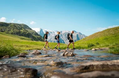 3 randonneurs marchent dans le aprc proche d'un lac, avec an arrière plan des montagnes enneigées